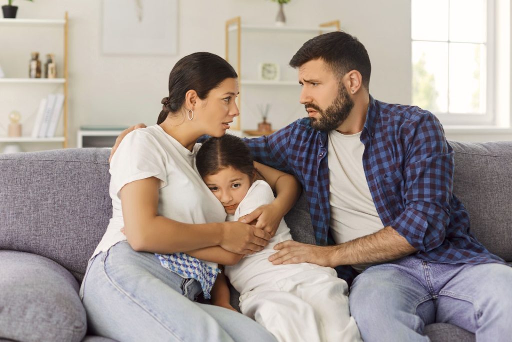 Streitende Eltern auf einer Coach zuhause mit ihrem Kind zwischen sich, welches sich an die Mama drückt – ganzheitliches Coaching für Familien in Chemnitz